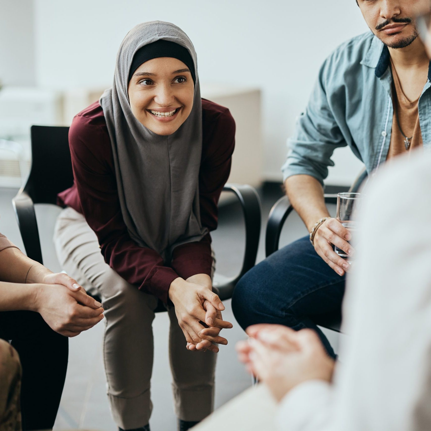 Group of diverse people having group meeting with their therapist at mental health center. Focus is on happy Muslim woman.
